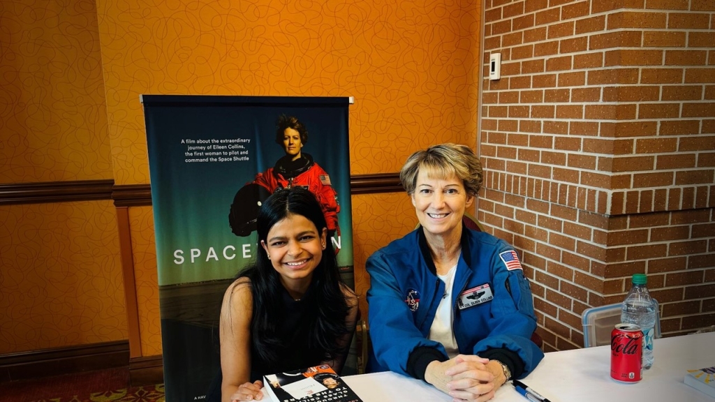Deepa Choudhry and Col. Eileen Collins sitting at table with Space Women poster behind them. 