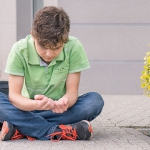 stock photo of child sitting on sidewalk with backpack