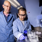 Two men standing by a table looking at lab equipment.