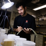 Young man standing in a laboratory in front of a light. He is holding a notebook and pen.