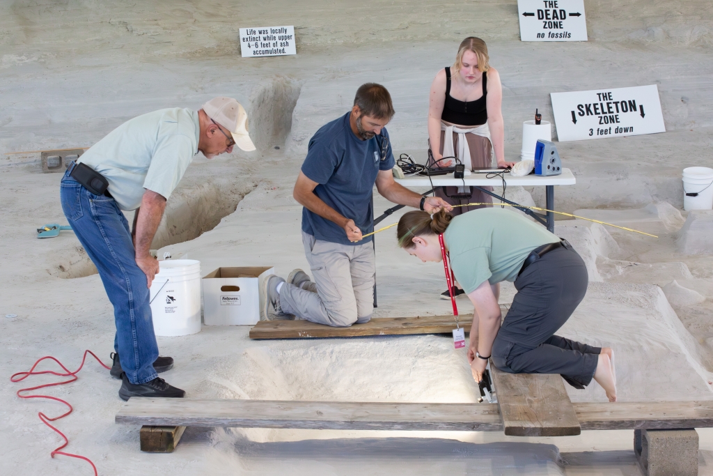 Four people gathered around 3D scanning equipment on the ash floor of the rhino barn, beneath signs reading “The Dead Zone” and “The Skeleton Zone.”