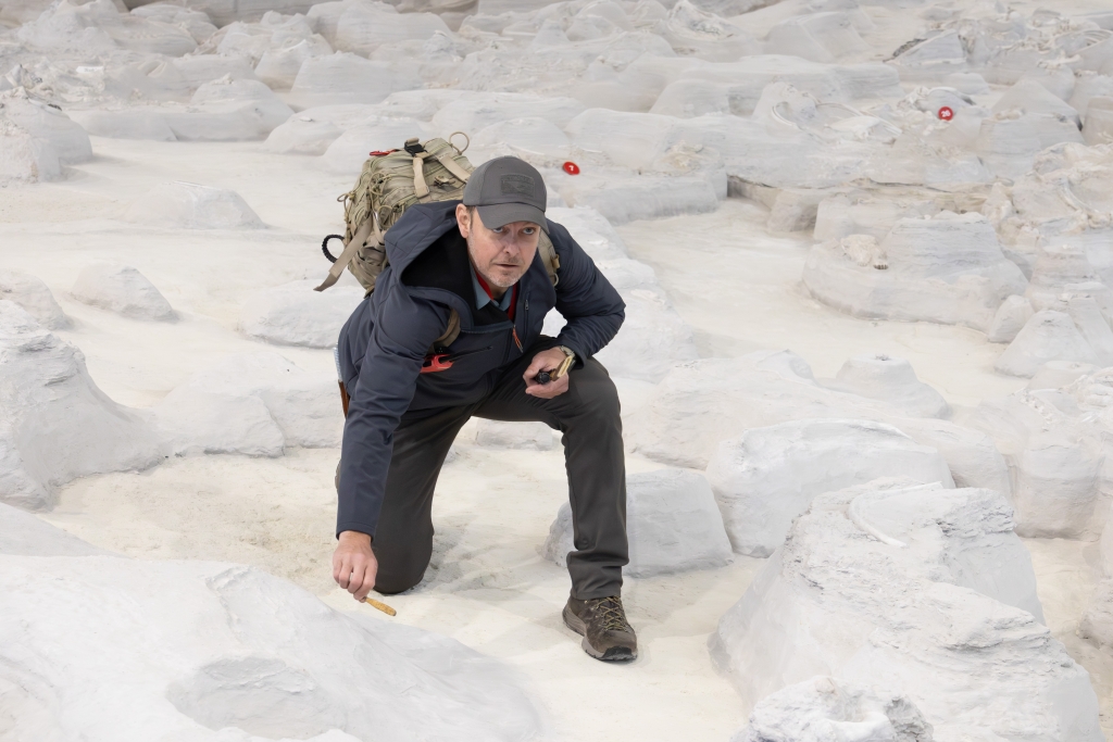 Sam Matson crouching on the pale ash surface of the rhino barn, tapping it with a small hand tool.
