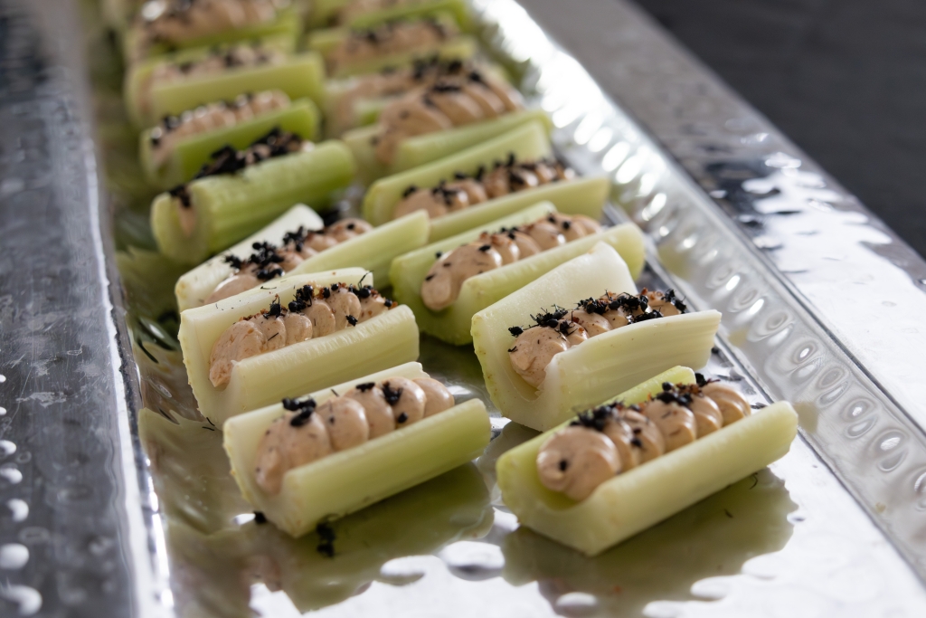 Pieces of green celery sit on a silver tray, complete with a piped-in cream cheese filling and black ants. A take on "ants on a log."