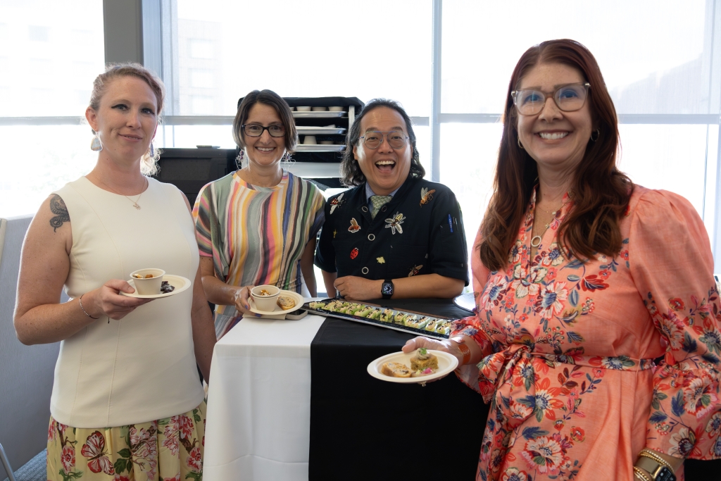 Chef Joseph Yoon, wearing an insect-embroidered jacket, laughing alongside three women holding small plates of insect appetizers.
