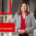 Women in gray blazer and red shirt, standing in front of a staircase